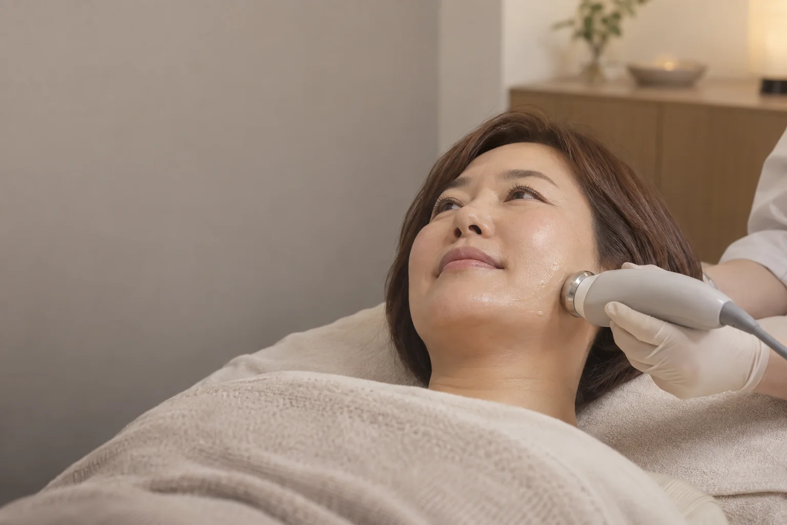 장갑을 착용한 관리자가 성인 모델의 턱선에 비침습 관리 기기를 적용하는 장면